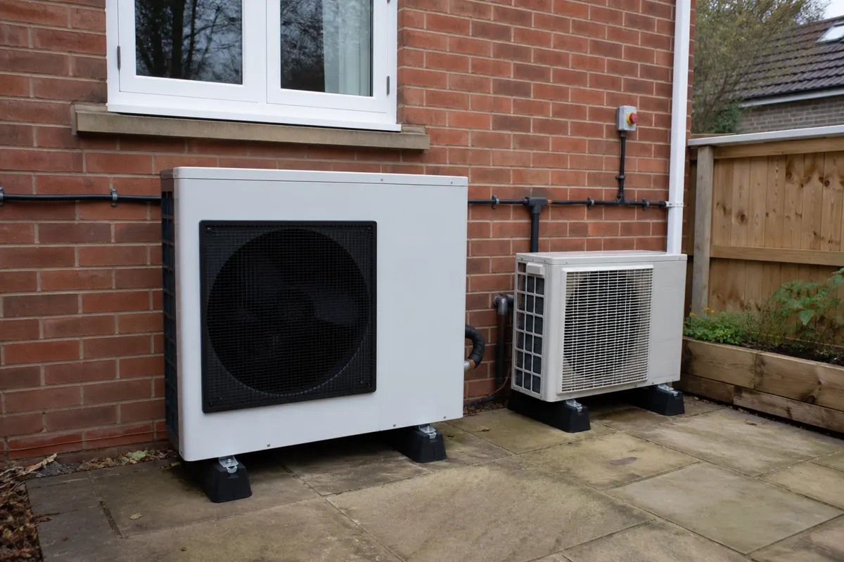Air-to-water heat pump outdoor unit beside a smaller split-system condenser on a UK brick house wall